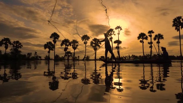 Silhouette of fishermen or fisherman throw fishing nets to catch fish at the pond in the sky morning. Slow motion footage of silhouette fisherman or fisher throwing a fishing net in yellow sky sunrise