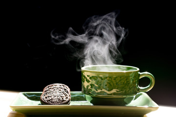 Obraz na płótnie Canvas Green cup of coffee with smoke and cookie isolated on dark background.