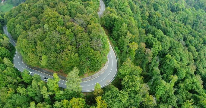 Mountain road in the woods with passing cars. Aerial view with forward movement.