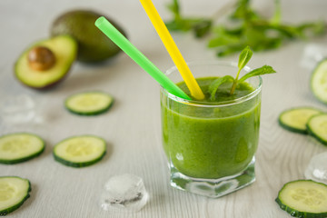 A glass of green vegetable smoothies on a white wooden background, and pieces of ice on the table