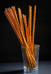 Pretzel sticks in small glass on black background - obrazy, fototapety, plakaty