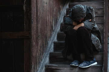 Homeless man sitting on the stairs of the old building andhe warms himself.  Problems of big modern...