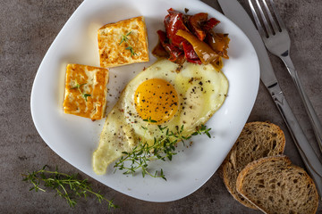 Fried egg with fried cheese, butter and some pickles on the plate