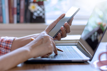 Casual businesswoman hand using mobile smartphone, work on laptop computer, browsing internet application in modern office. 