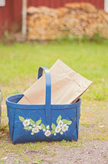 A blue basket on the ground. A red barn and logs on the background.