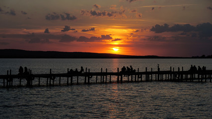 group of unrecognizable people in silhouette sitting on jetty pier watching sunset sundown at lake Steinhuder Meer in Germany