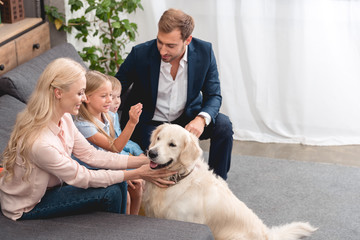 high angle view of happy young family petting dog while sitting on couch at home