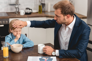 young father checking temperature of son with hand during breakfast