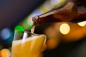 Motion of beer pouring from bottle into glass on bokeh light night background drinking alcohol...