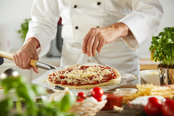 Chef sprinkling mozzarella cheese onto a raw pizza