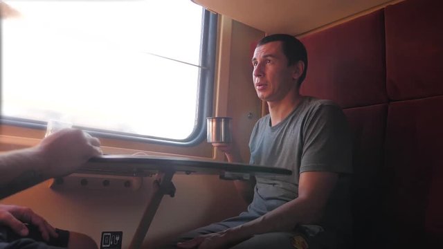 man is sitting on the train carriage holding a Railway and drinking coffee and tea. slow motion video. two men drinking tea on the train talking the train lifestyle social media . man with smartphones