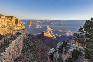 Golden sunlight and hazy clouds in the  famous Grand Canyon rock formations on a hiking trail