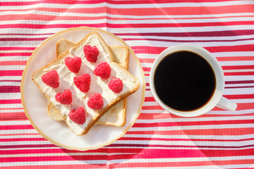 Toast with curd cheese and raspberries and cup of coffee or chicory on background of bright striped napkin