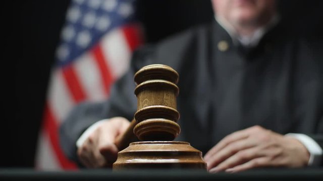Judge's hand with wooden gavel hammering against American flag in United States court