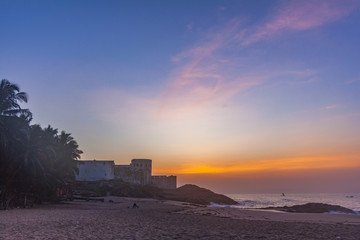 Fototapeta na wymiar Colourful morning sky on the beach of Cape Coast, Ghana. Sunrise over an old castle and the ocean