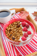 still life: granola with raspberries, coffee and autumn leaves on bright striped napkin