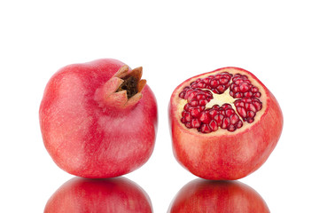 Cut and whole red pomegranates with seeds on white mirror background with reflection isolated close up