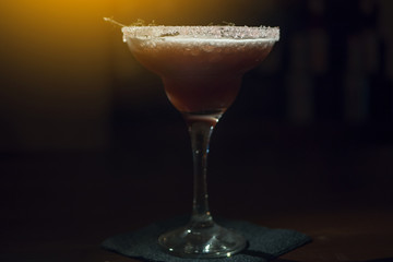 Cocktail in a beautiful glass on the table. In a dark bar