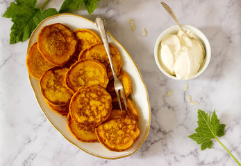 Homemade pumpkin pancakes served with sour cream on a light background.