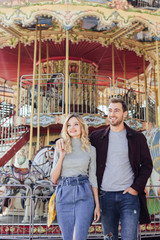 affectionate couple in autumn outfit hugging near carousel in amusement park
