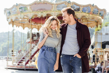 smiling couple in autumn outfit walking and hugging near carousel in amusement park © LIGHTFIELD STUDIOS