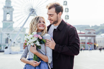 boyfriend hugging girlfriend with bouquet in city