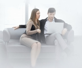 two employees of the company work on a laptop, sitting near a window in the office