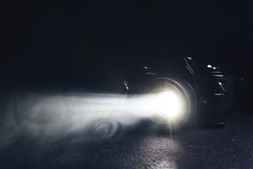 old camera with a ray of light from the lens in the smoke on a black background
