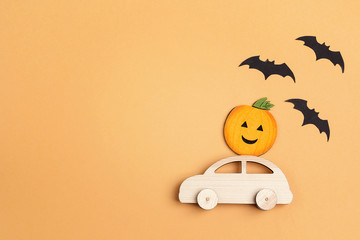 Wooden toy car with funny pumpkin on the roof and bats on orange background. Space for text.