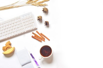 Women's designer's work place/ Cup of tea, purple pen, notepad, computer, dry autumn herbs, pine cones and rocking horse on a white table. Flat lay style office photography