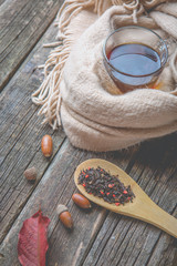 Autumn composition, glass cup of tea and a warm scarf on wooden table background.