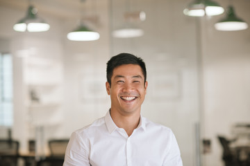 Young Asian businessman laughing while standing in a modern office