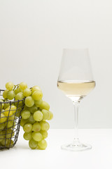 Copa de vino blanco con uvas verdes sobre un fondo claro. Vista de frente y de cerca. Copy space. Formato vertical