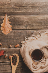 Autumn composition, glass cup of tea and a warm scarf on wooden table background.