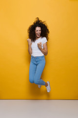 Fototapeta na wymiar Full length photo of positive woman 20s with curly hair having fun and jumping, isolated over yellow background