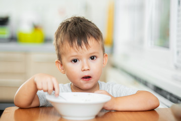 charming child in the kitchen eating oatmeal