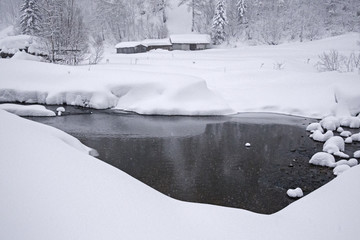 Winter landscape with lake and some houses submerged by heavy snowfall.