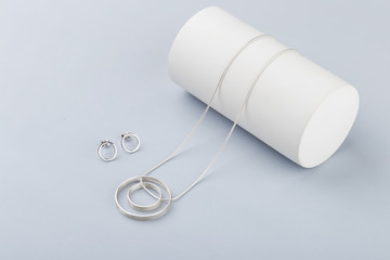 Minimalist geometric silver necklace and circle stud earrings on gray background
