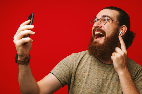 Happy man with beard listening music at airpods over red background