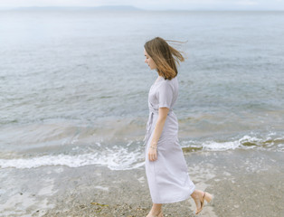 Woman in dress enjoys a walking near the sea shore.