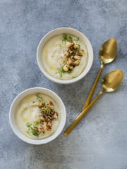 Cauliflower cream soup , decorated with fried cauliflower inflorescence in white bowls with golden spoons on a gray background. Top view