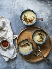 Cauliflower cream soup  in three blue bowls, decorated with fried cauliflower inflorescence, red paprika powder and vintage spoons on a gray background and wooden tray. Top view. 