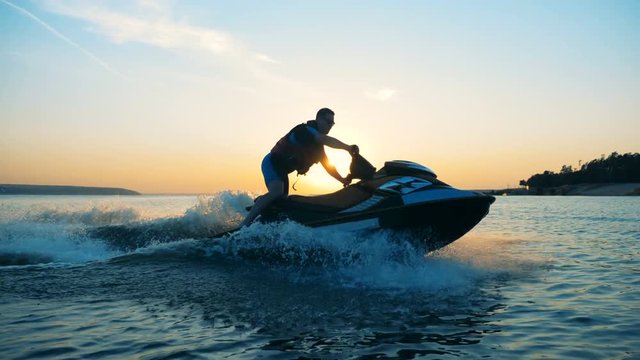 Person drives on a waverunner on a sunset background, side view.