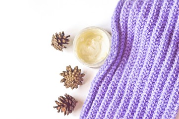 Winer skin care/ Jar nourishing cream for skin care, purple wool scarf and pine cones. Autumn and winter skin care. Flat lay beauty photo