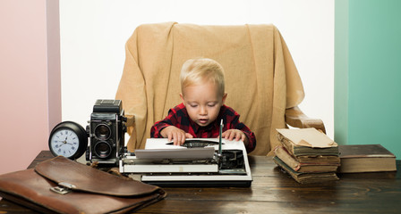 Fototapeta na wymiar Small kid typewrite paper on retro typewriter at desk. Boy typewrite keys on vintage machine