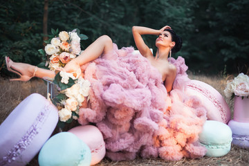 Fashion sexy woman dressed in pink stunning dress surrounded of French Macarons