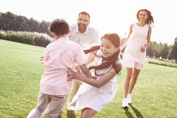 Fototapeta premium Bonding. Family of four running on grassy field playing playing 