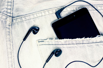 Closeup to jeans pocket with smartphone and headphones. toned.