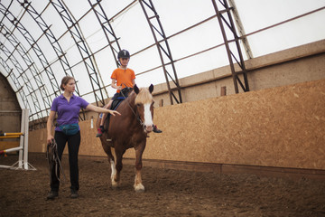 Boy in helmet learning Horseback Riding with instructor