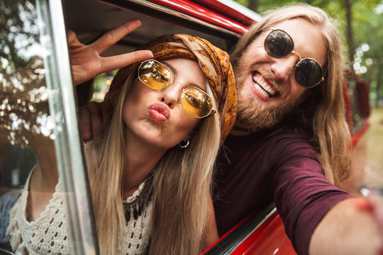 Photo of kind hippie couple smiling, and showing peace sign while driving retro minivan in forest